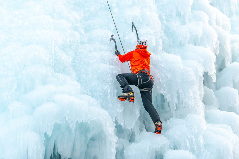 Man with climbing equipment, ice axes and rope, hiking at a frozen waterfall
