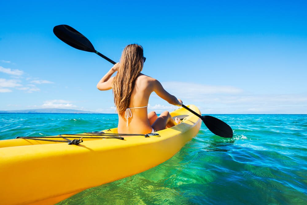 woman kayaking in a yellow kayak on brilliant clear water