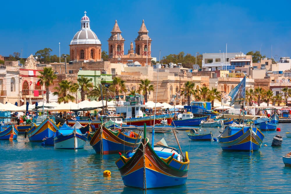 Colorful boats in a harbor in Malta with architecture behind
