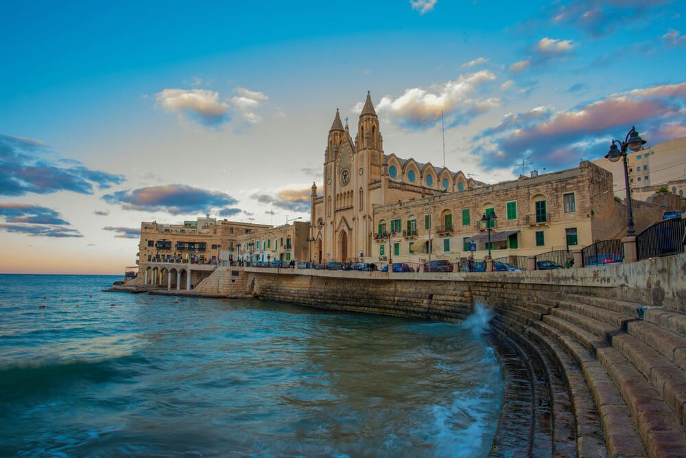 Panorama of Balluta Bay and Neo-Gothic Church of Our Lady of Mount Carmel, Balluta parish church, during evening blue hour in Saint Julien, Malta