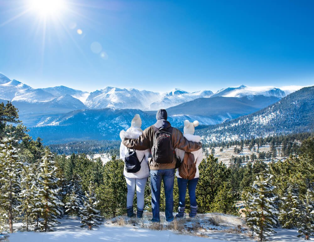 Happy family with arms around each other enjoying beautiful mountain view on winter hiking trip in Rocky Mountain National Park.