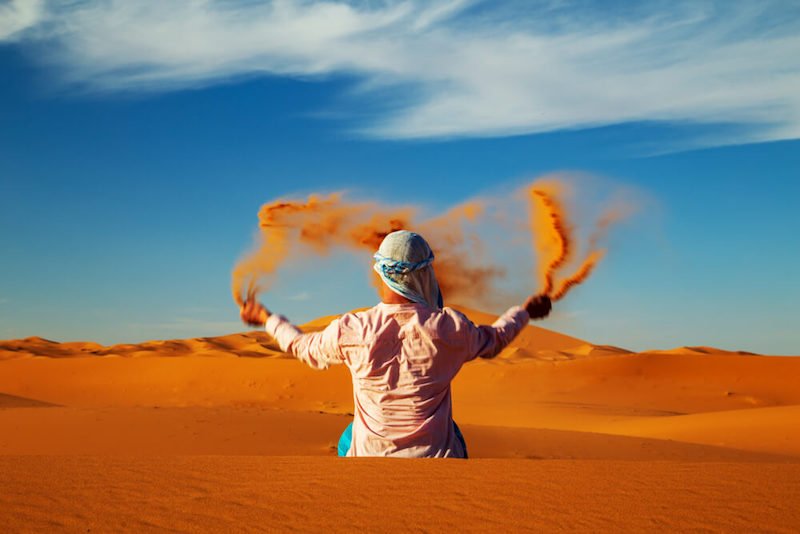 a person with a hat on throwing sand in the sahara desert