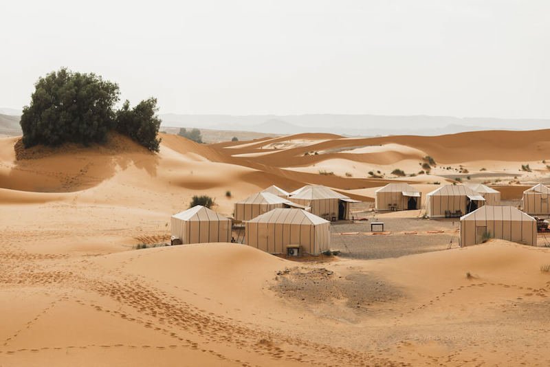 Eco tents in a glampsite in Morocco with views of the dunes and some desert shrubbery on a hazy day.