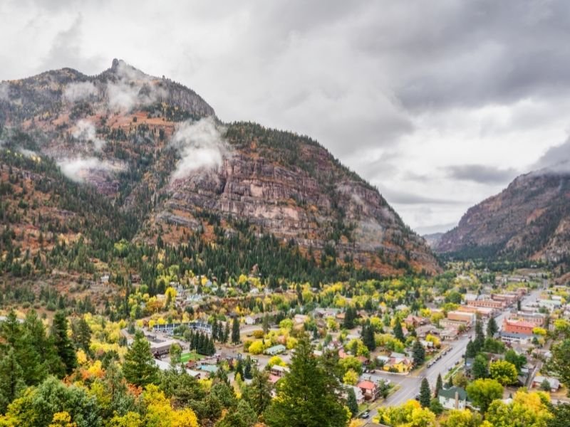 the town of ouray at the base of mountains with some trees starting to turn yellow in the fall