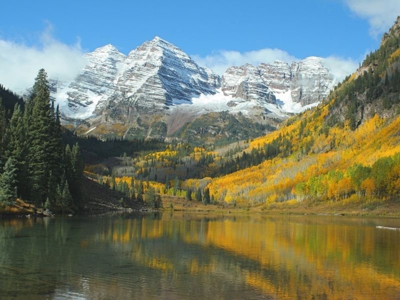 yellow aspens and evergreen trees reflecting in maroon lake like a painting with the snow-capped mountains behind it in autumn in colorado