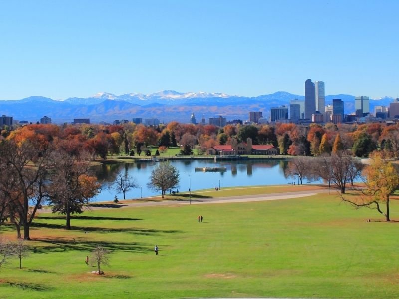 green grassy park field with colorful orange and red trees and a manmade lake in denver colorado in the fall