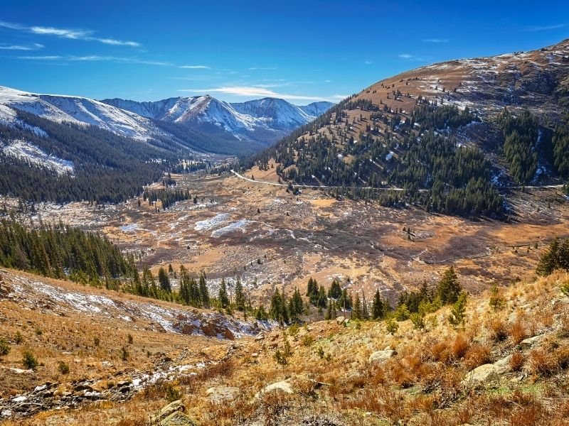 driving through the mountain pass of independence pass with road, yellow trees, light snow and mountains in the fall in colorado