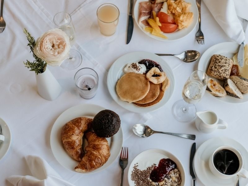 a breakfast spread on a white tablecloth with pastries and coffee and pancakes