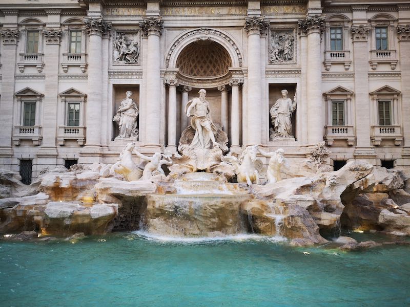 The beautiful symmetry of the Trevi fountain with blue water and ornate marble sculpture work