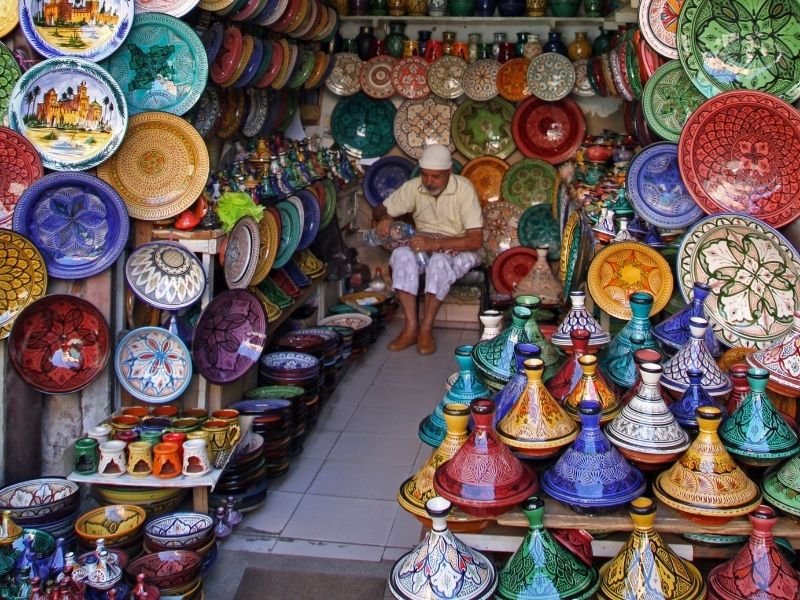 man wearing a white hat in a shop selling colorful ceramic plates in marrakech medina