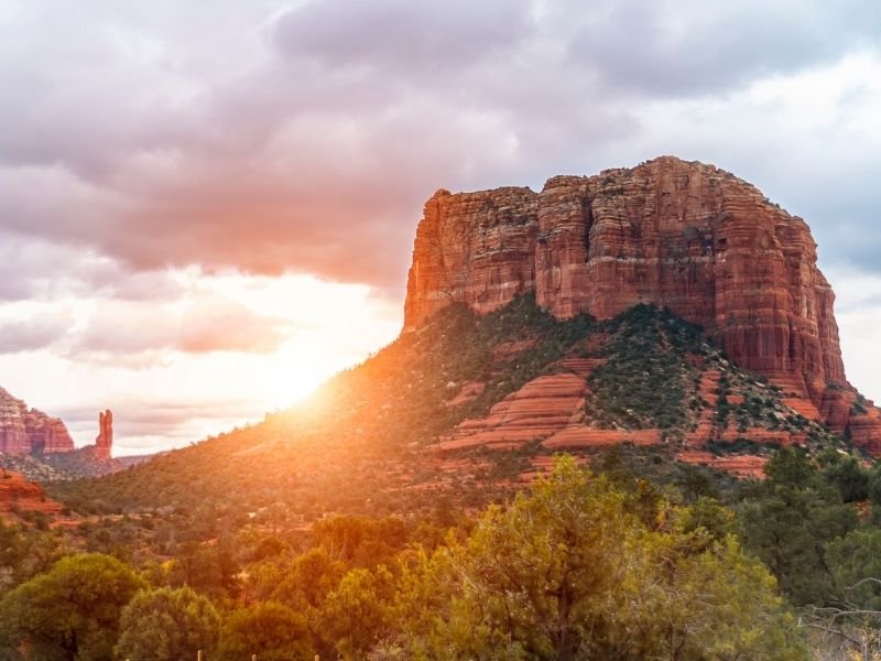 Sun rising over the red rocks of Sedona, with lots of clouds in the sky, showing a perfect warm weather getaway in the USA