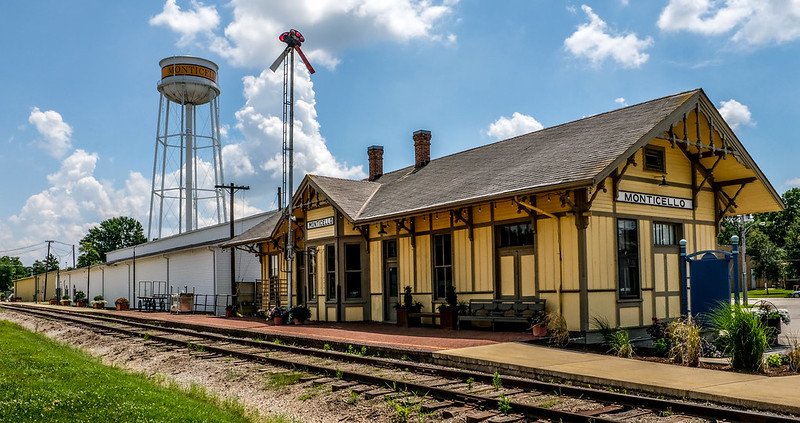 a yellow painted train depot with a large water silo in the background in monticello illinois small town