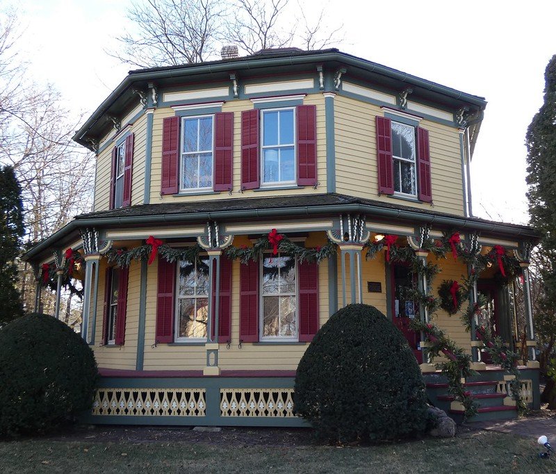 a yellow painted octagonal shaped house with red shutters and christmas decorations