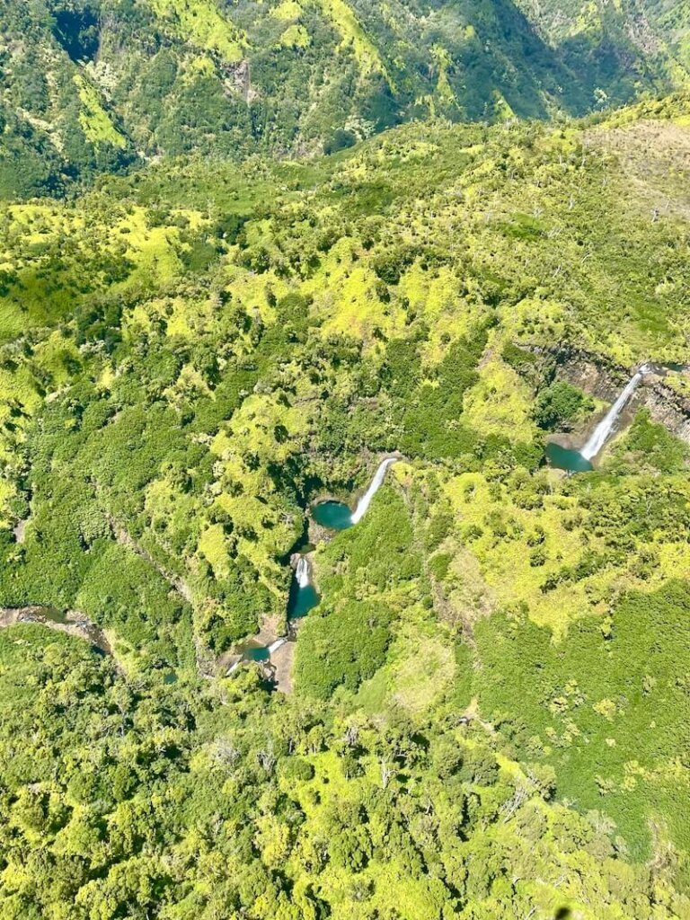 Several waterfalls cascading through the Kauai landscape with brilliant turquoise poools at each waterfall base