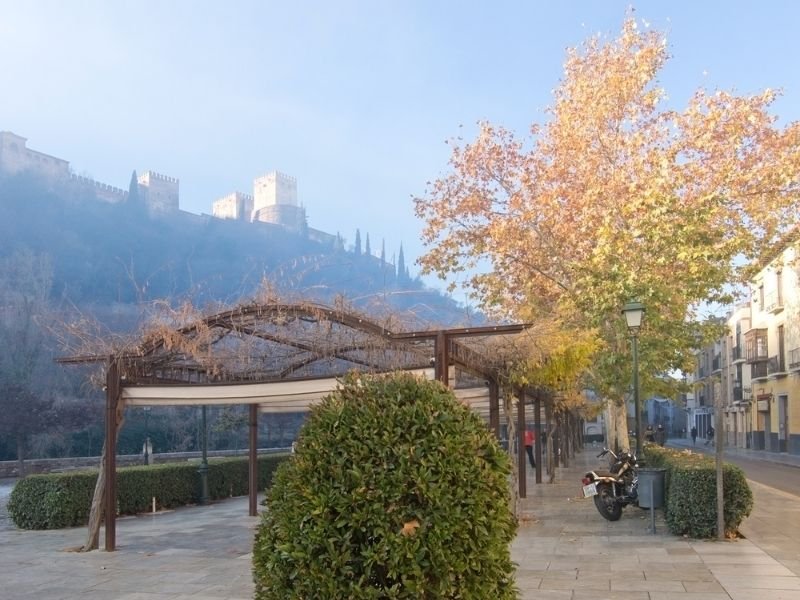 view of the paseo de los tristes and looking up at the alhambra from a plaza area with trees and motorcycles