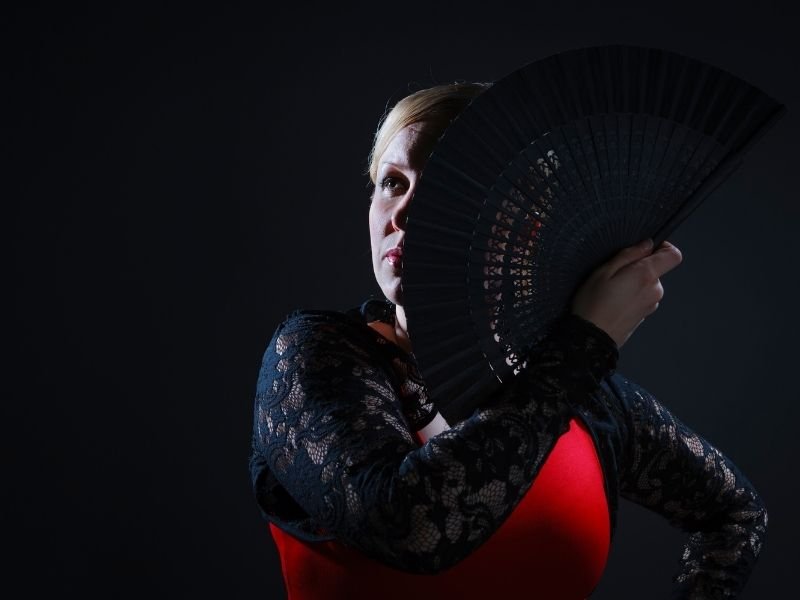 woman performing in a flamenco show with a fan in front of her face