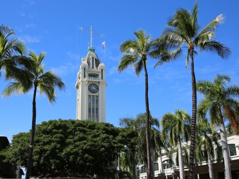 the famous aloha tower, a former lighthouse turned landmark and mixed use building with restaurants and residences, amongst palm trees and blue sky