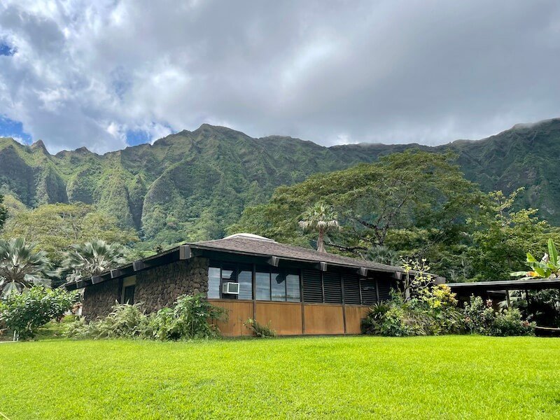 the visitor center at the botanic garden in oahu with rugged cliffs behind it