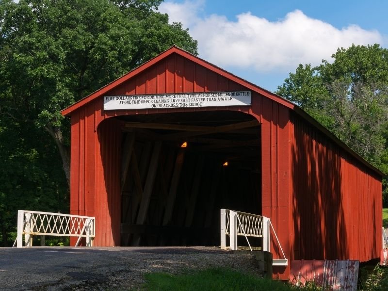 historic red covered bridge with side siding and a sign that reads five dollars fine for driving more than twelve horses across this bridge