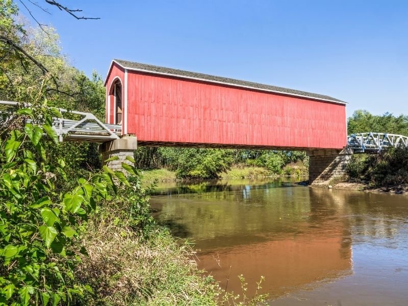 a view of princeton's famous red covered bridge as seen from the side spanning the river with greenery around it