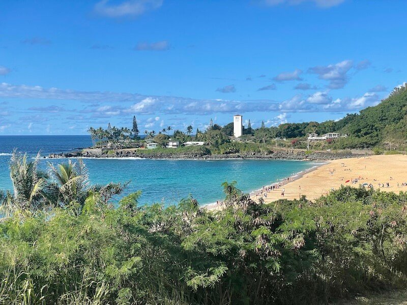 view of the waimea beach with a white lighthouse in the distance