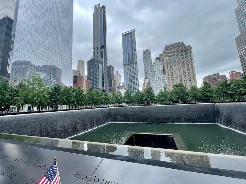 names engraved in the wall around the memorial for the victims of 9/11 with an american flag on a gray gloomy day