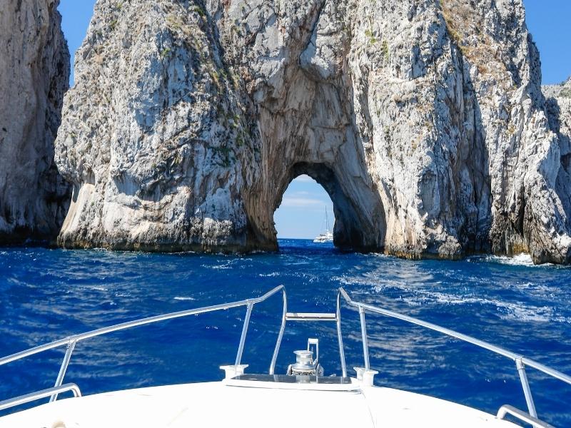 a boat going towards a natural arch off of the coast of capri