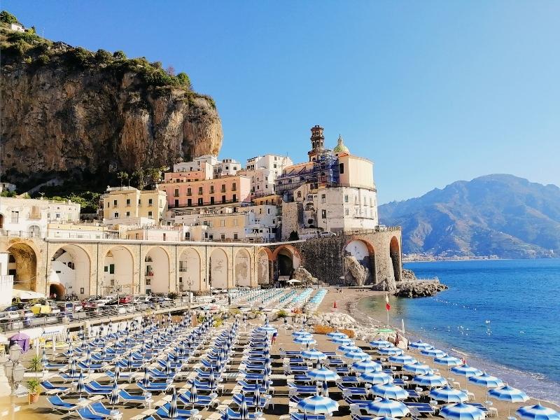 the umbrellas on the beach at atrani with the town in the background on the amalfi coast