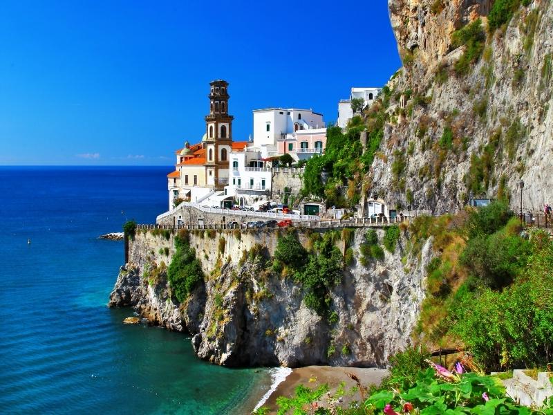 the small town of atrani italy with some cars on the road and a small beach and blue waters