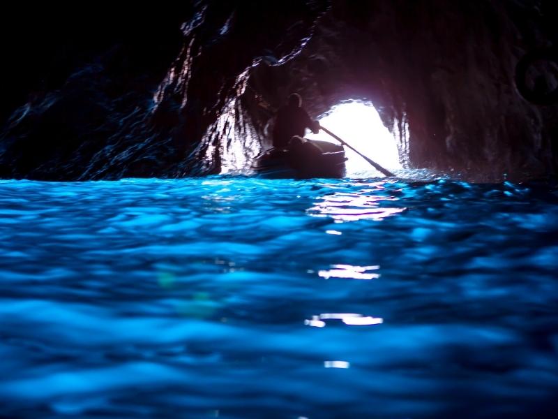the intense color of the blue water in the blue grotto with a man in a small boat leaving the cave