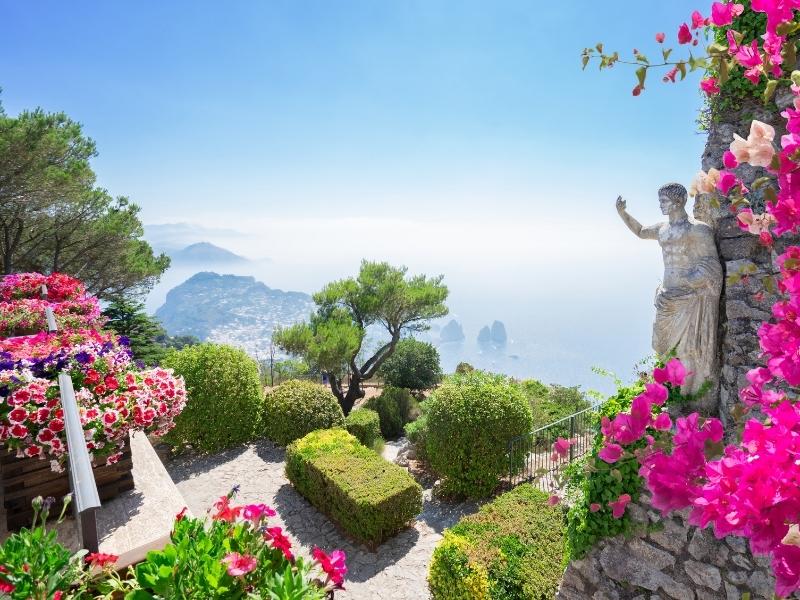 gardens in upper capri with view of flowers, statue, and sea stacks below