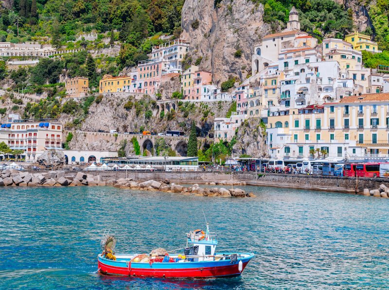 a red and blue fishing boat in the water near the town of amalfi in the central part of the amalfi coast in italy