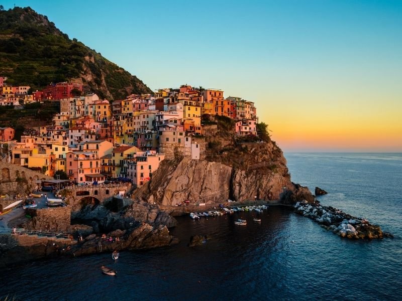 the town of manarola at sunset with beautiful colors on the horizon and the town washed in golden light with colorful houses