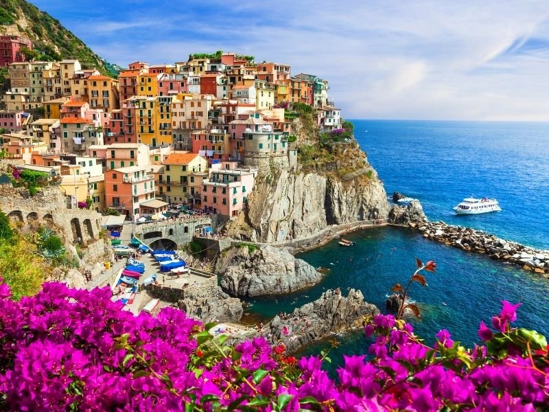 the cinque terre area of italy not too far from milan - a good addition to a milan itinerary. colorful houses perched on a seaside cliff with flowers and harbor.