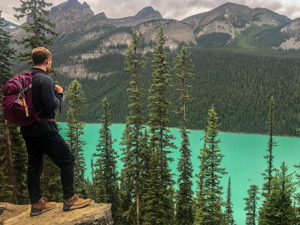 man with hiking shoes and backpack looking over lake Louise while using a hiking app called all trails to navigate through the trails of the Canadian rockies