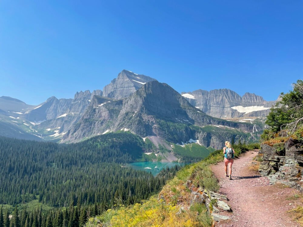 Kassidy travel blogger walking the trail at Grinnell Lake in Glacier National Park in Montana while using a popular hiking app called the Hiking Project