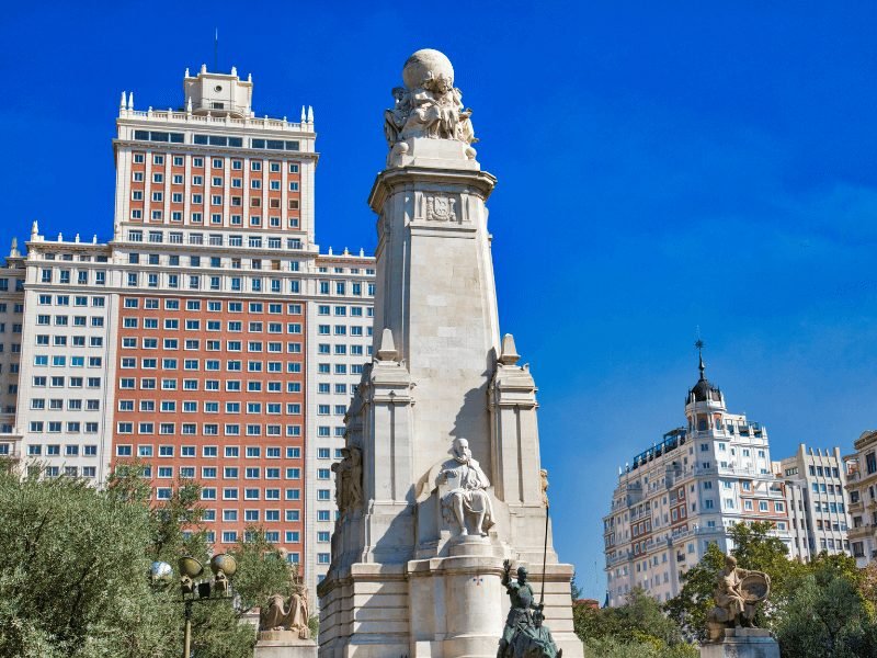 view of the statue of miguel de cervantes the author of don quixote in front of several large skyscrapers in the madrid skyline