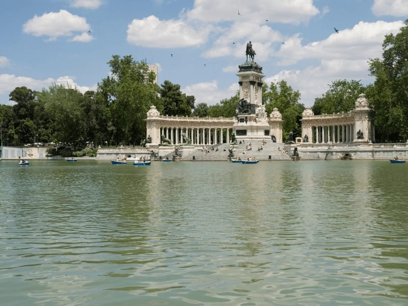 small little rowboats out enjoying the retiro park lake with the famous alfonso xii statue at the head of the lake in retiro park in madrid