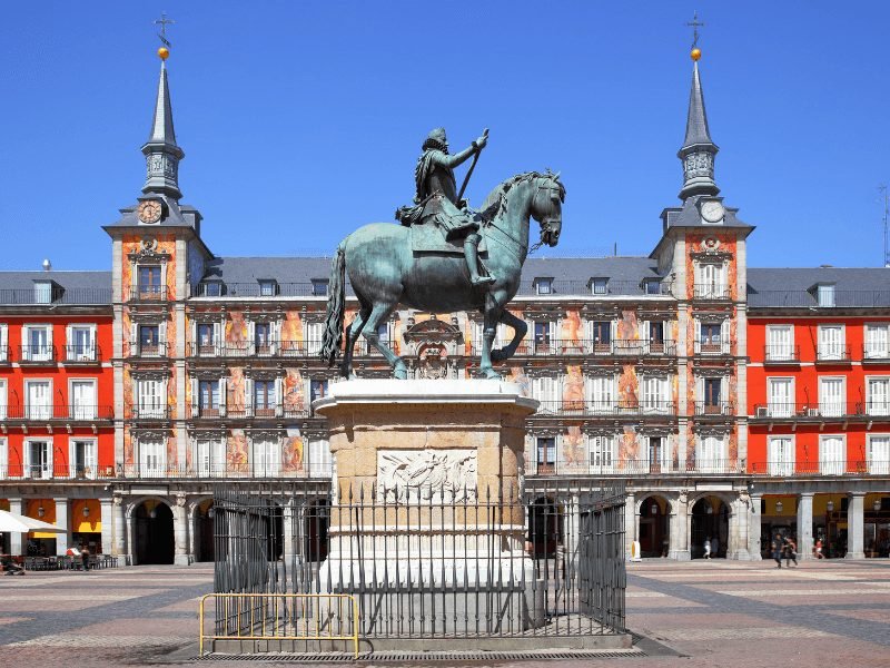 a horse statue in front of the famous facade buildings of plaza mayor one of the busiest places for people watching in madrid 