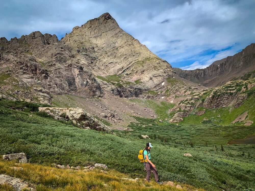 Female hiker with yellow backpack and teal shirt and hat hiking in Colorado while using a popular hiking app