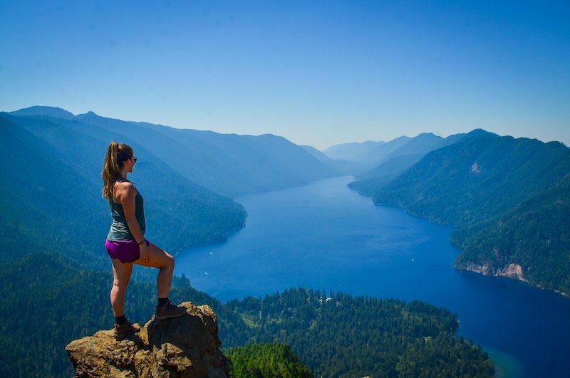 hiker at mt storm king looking over the scenery wearing a tank top and shorts while using the weather app to plan a hike