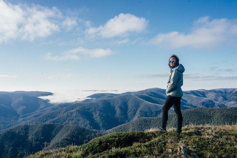 traveler wearing a silver jacket and leggings smiling at the camera while backpacking in the mountains