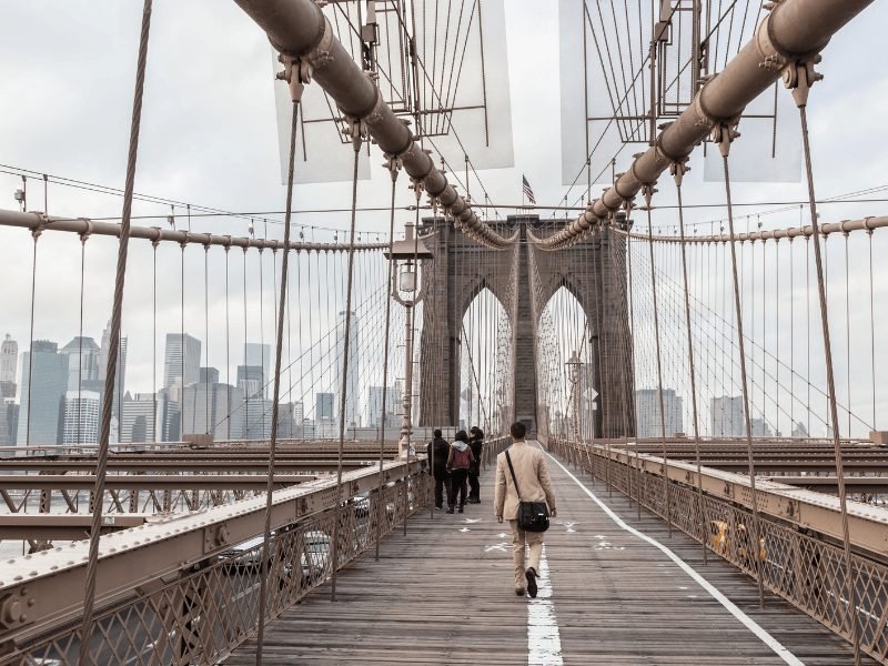 man walking across the brooklyn bridge in the morning light