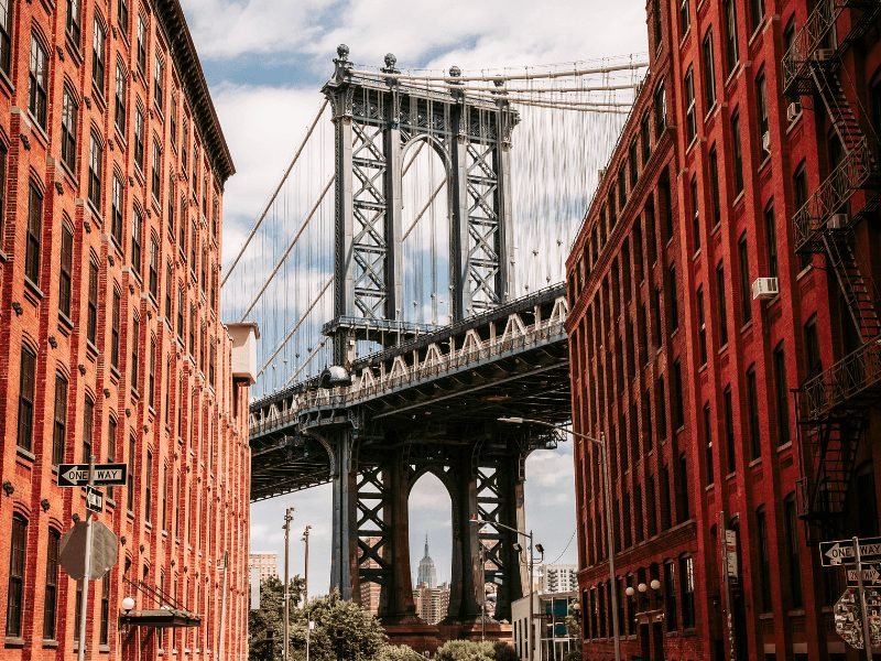 the manhattan bridge seen between two red buildings, an iconic sight in dumbo