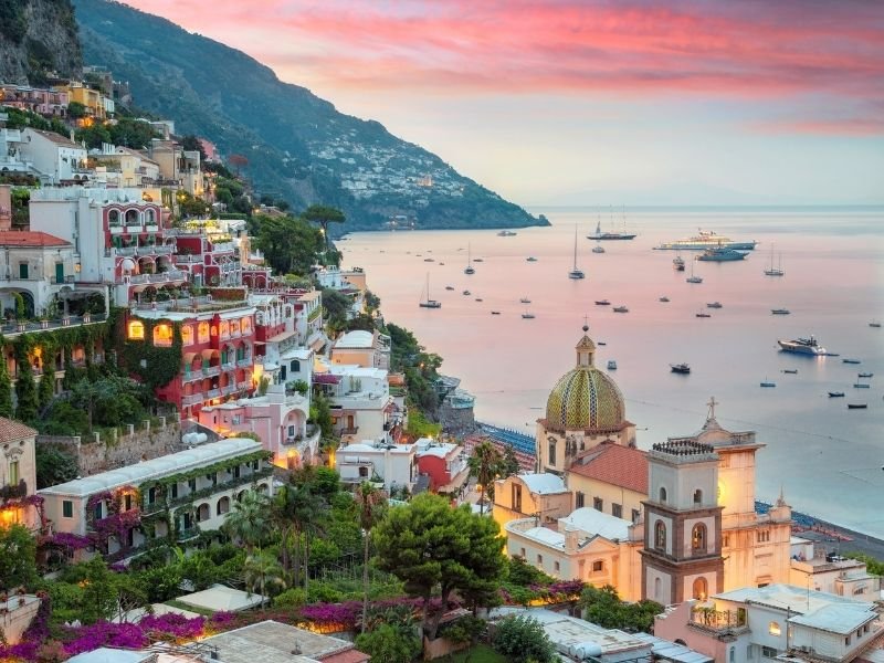 view of the town of positano at sunset on the amalfi coast with lots of boats in the water and colorful views