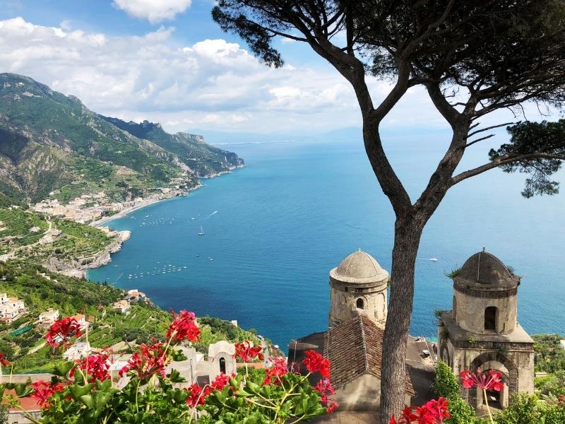 the charming seascape of ravello on the amalfi coast with red flowers, an old church, terraced landscape, and tree with water with boats below