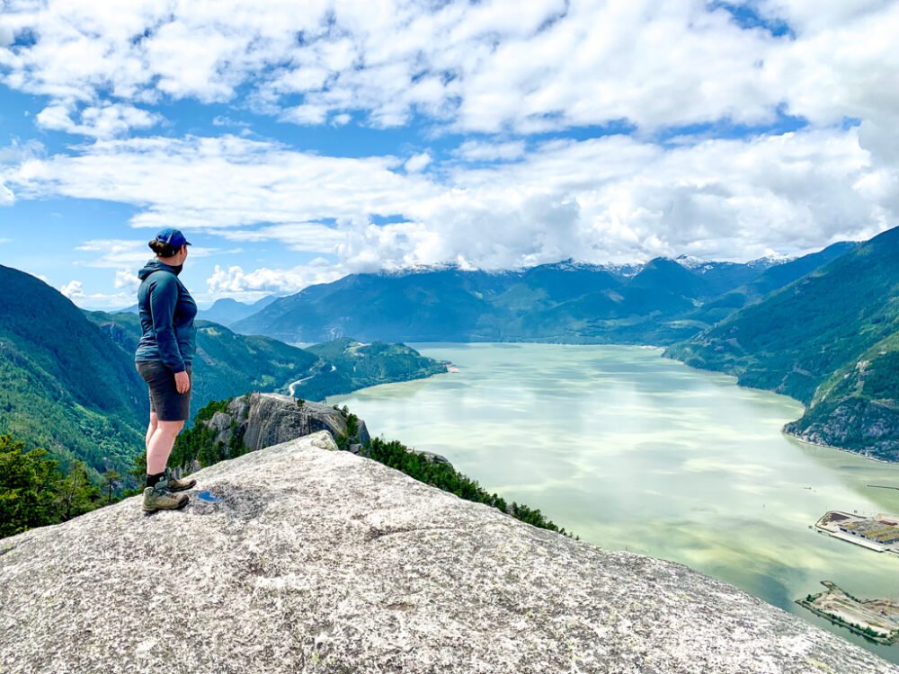 Hiker standing on a rock overlooking a view as she uses a hiking app called Trailforks to guide the way through the landscape of British Columbia, Canada