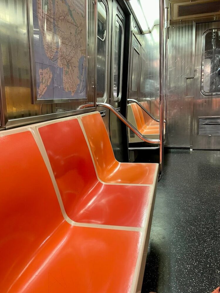 orange seats and black and white speckled floor of the new york city subway on an older car