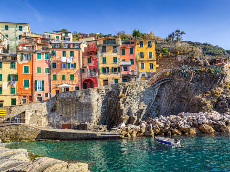 blue waters, boat, and colorful houses typical of cinque terre on a sunny day, with laundry out on a line
