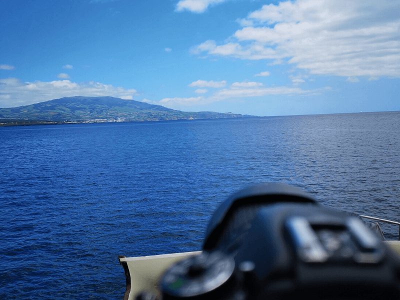 blurry part of boat with view of island of azores in distance while on a whale watching tour